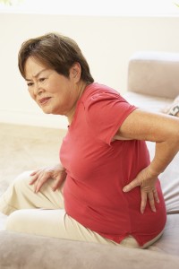 Woman with lower back pain putting hands on lower back and grimacing