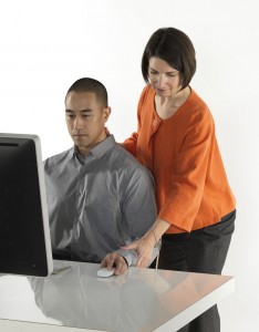 Alexander Technique teacher standing, helping a man with his posture at a laptop
